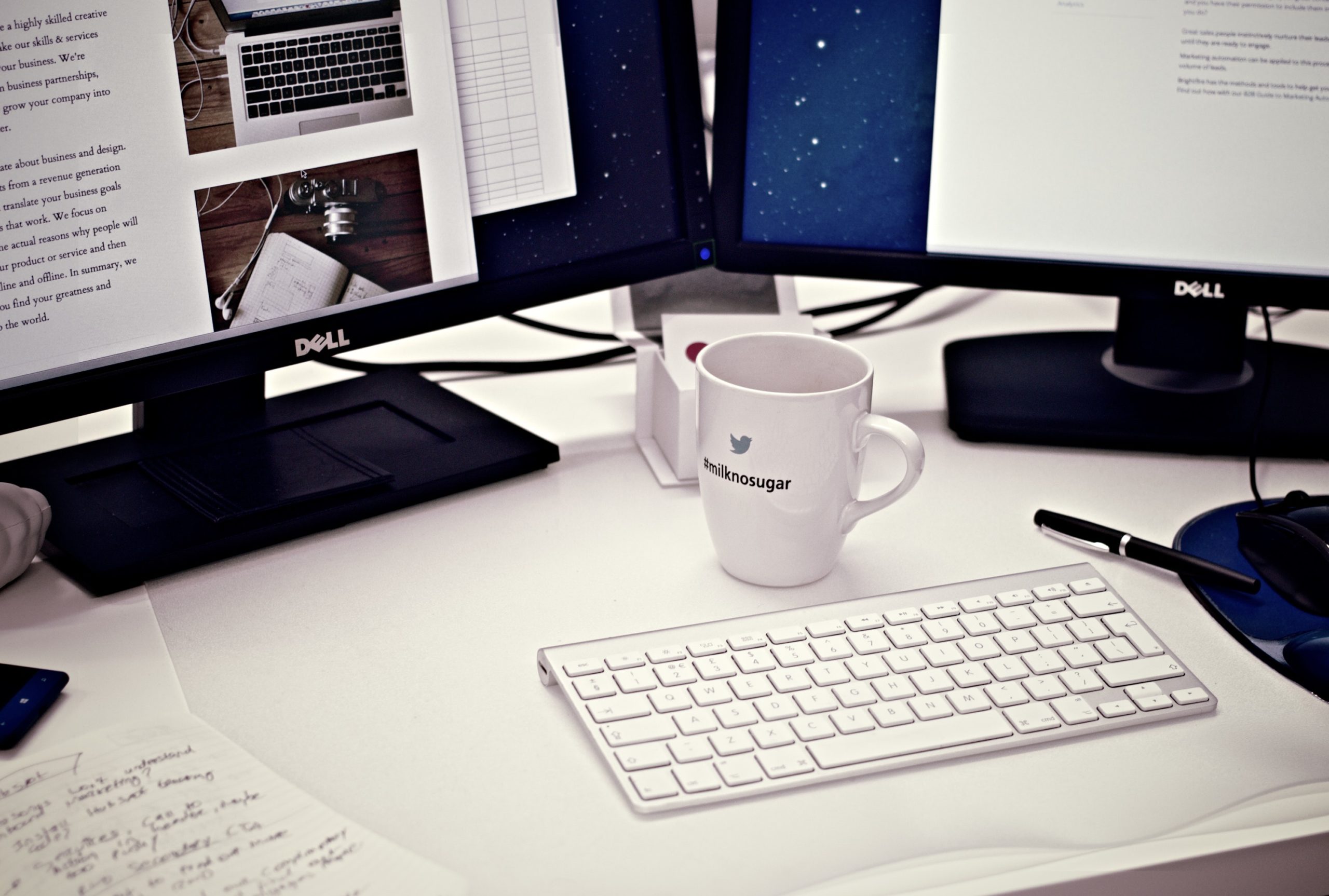 white mug and keyboard in front of two desktop monitors